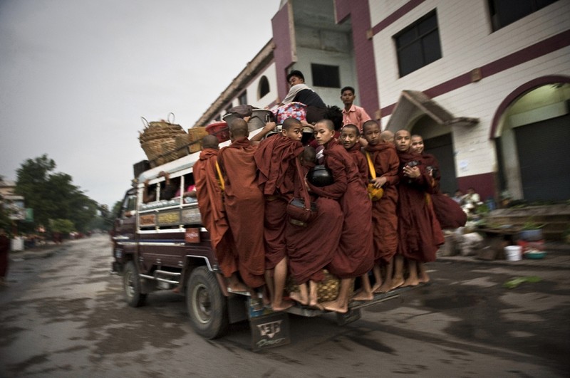 Буддийские послушники на задней части автобуса едут собирать милостыню на рассвете