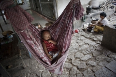 Ребенок спит в гамаке, в то время как его мать готовит обед в доме на вершине холма