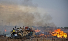 Грузовик с ворованными вещами на фоне горящих хижин в центре города Абайи, Судан. Десятки тысяч суданцев бегут из неспокойного с