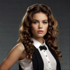 Image is a high-fashion portrait featuring a woman with voluminous, curly brown hair styled dramatically