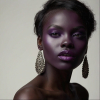 Image is a high-fashion portrait photograph featuring a person with dark skin and striking facial features